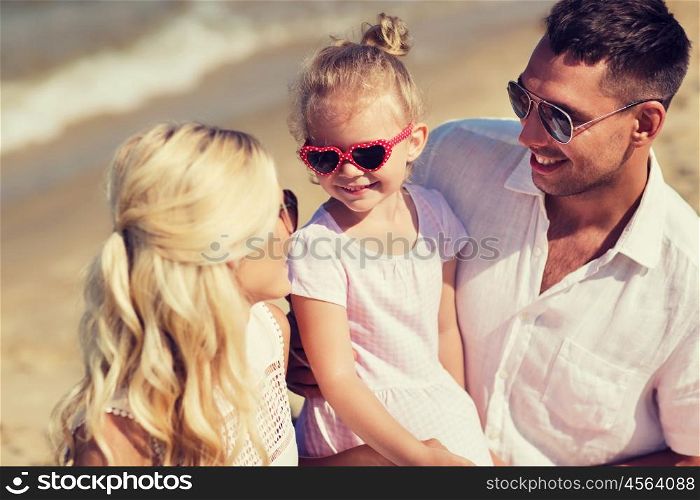 family, vacation, adoption and people concept - happy man, woman and little girl in sunglasses talking on summer beach
