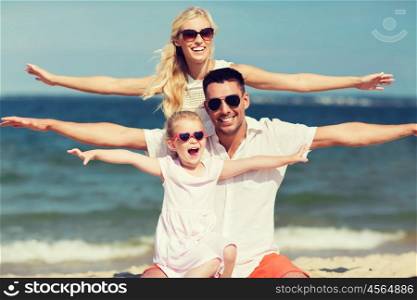 family, vacation, adoption and people concept - happy man, woman and little girl in sunglasses having fun on summer beach