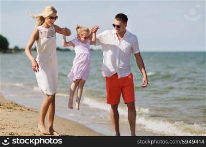 family, vacation, adoption and people concept - happy man, woman and little girl in sunglasses walking on summer beach