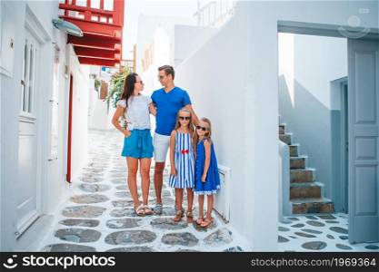 Family vacation in Europe. Parents and kids at street of typical greek traditional village with white walls and colorful doors on Mykonos Island, in Greece. Family vacation in Europe. Parents and kids at street of typical greek traditional village with white walls and colorful doors on Mykonos Island