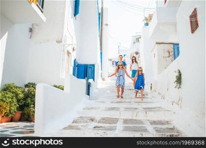 Family vacation in Europe. Parents and kids at street of typical greek traditional village with white walls and colorful doors on Mykonos Island, in Greece. Family vacation in Europe. Parents and kids at street of typical greek traditional village with white walls and colorful doors on Mykonos Island