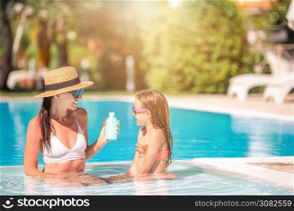 Family vacation. Young mother applying sun cream to kid in swimming pool. Young mother applying sun cream to daughter nose