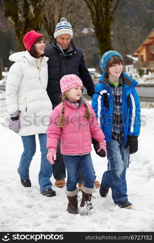 Family Walking Along Snowy Street In Ski Resort