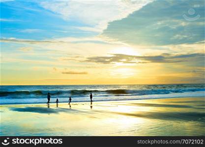 Family walking at sandy beach, sunset seascape, Bali, Indonesia