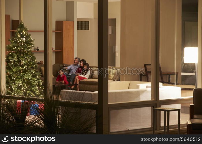 Family Watching Christmas TV At Home Viewed From Outside
