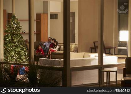 Family Watching Christmas TV At Home Viewed From Outside