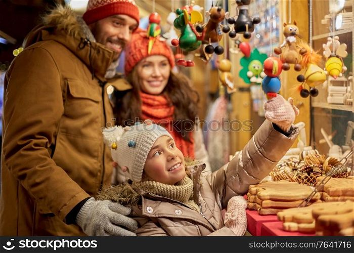 family, winter holidays and celebration concept - happy mother, father and little daughter choosing souvenirs at christmas market on town hall square in tallinn, estonia. happy family buying souvenirs at christmas market