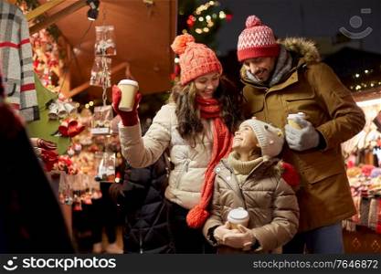 family, winter holidays and celebration concept - happy mother, father and little daughter with takeaway drinks at christmas market on town hall square in tallinn, estonia. family with takeaway drinks at christmas market