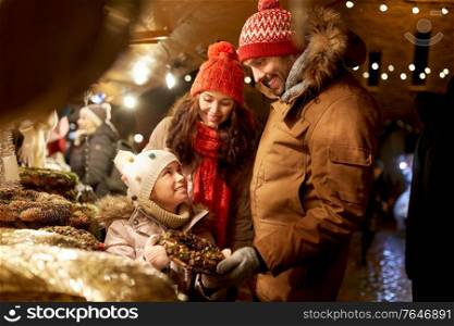 family, winter holidays and celebration concept - happy mother, father and little daughter buing wreath at christmas market on town hall square in tallinn, estonia. happy family buing wreath at christmas market