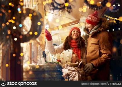 family, winter holidays and celebration concept - happy mother, father and little daughter at christmas market on town hall square in tallinn, estonia over lights. happy family at christmas market in city
