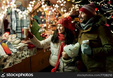 family, winter holidays and celebration concept - happy mother, father and little daughter with takeaway drinks at christmas market on town hall square in tallinn, estonia over lights. family with takeaway drinks at christmas market