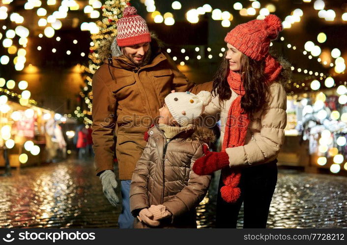 family, winter holidays and celebration concept - happy mother, father and little daughter at christmas market on town hall square in tallinn, estonia. happy family at christmas market in city