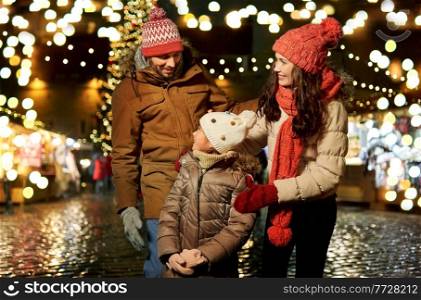 family, winter holidays and celebration concept - happy mother, father and little daughter at christmas market on town hall square in tallinn, estonia. happy family at christmas market in city
