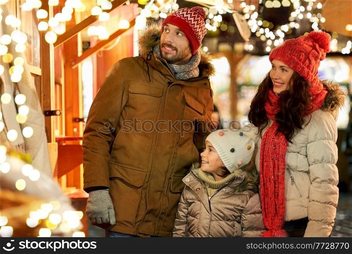 family, winter holidays and celebration concept - happy mother, father and little daughter at christmas market on town hall square in tallinn, estonia. happy family at christmas market in city