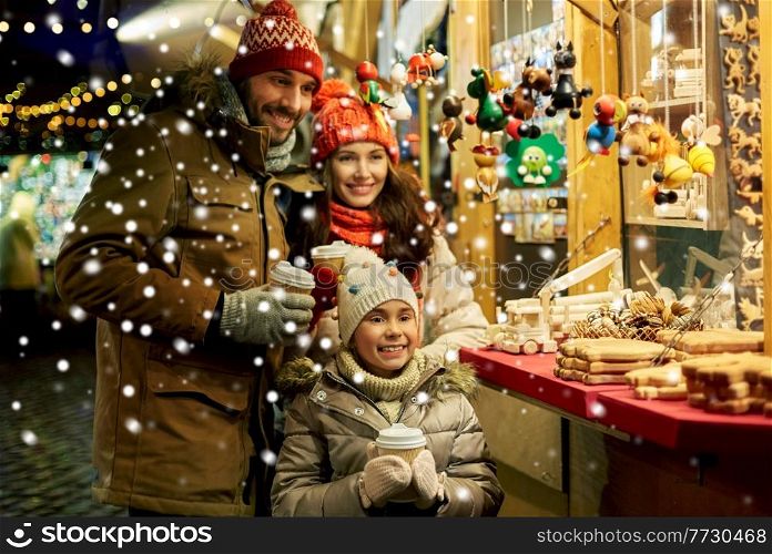 family, winter holidays and celebration concept - happy mother, father and little daughter with takeaway drinks at christmas market on town hall square in tallinn, estonia over snow. family with takeaway drinks at christmas market