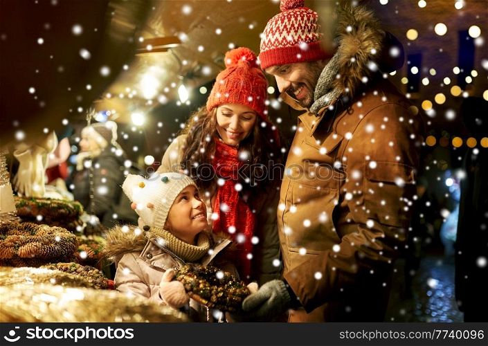 family, winter holidays and celebration concept - happy mother, father and little daughter buying wreath at christmas market on town hall square in tallinn, estonia over snow. happy family buying wreath at christmas market