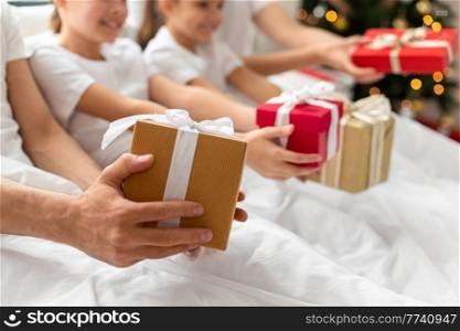 family, winter holidays and people concept - close up of happy mother, father and two daughters with christmas gifts in bed at home. family with christmas gifts in bed at home