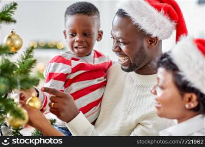 family, winter holidays and people concept - happy african american mother, father and little son decorating christmas tree at home on. happy family decorating christmas tree at home