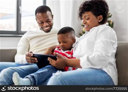 family, winter holidays and people concept - happy african american mother, father and baby son with tablet pc computer at home on christmas. african family with tablet pc on christmas