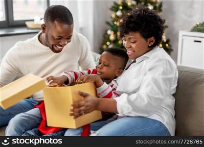 family, winter holidays and people concept - happy african american mother, father and baby son opening gift box at home on christmas. african family opening christmas gift at home