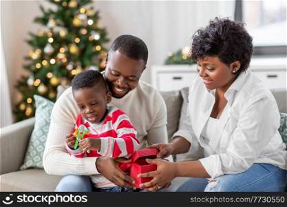 family, winter holidays and people concept - happy african american mother, father and baby son opening gift box with toy at home on christmas. african family opening christmas gift at home
