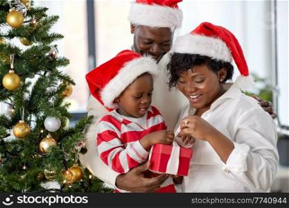 family, winter holidays and people concept - happy african american mother, father and little son opening gift box at home on christmas. african family opening christmas gift at home