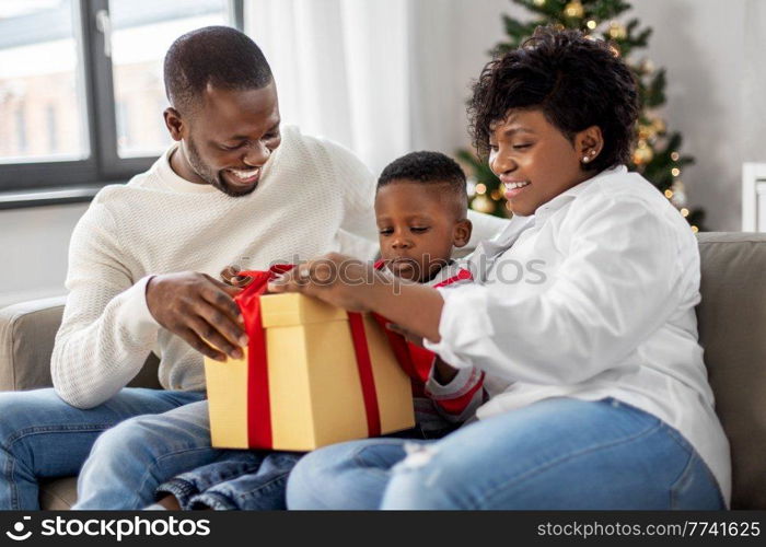 family, winter holidays and people concept - happy african american mother, father and baby son opening gift box at home on christmas. african family opening christmas gift at home