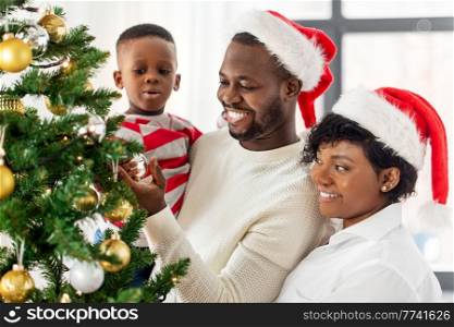 family, winter holidays and people concept - happy african american mother, father and baby son decorating christmas tree at home on. happy family decorating christmas tree at home