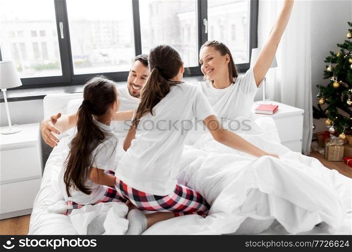 family, winter holidays and people concept - happy daughters wake their mother and father in christmas morning. happy children wake their parents on christmas