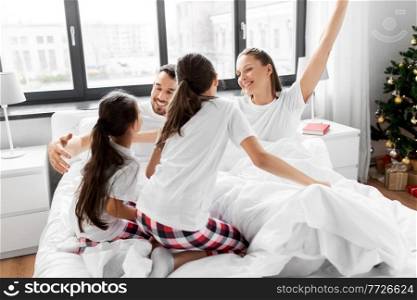 family, winter holidays and people concept - happy daughters wake their mother and father in christmas morning. happy children wake their parents on christmas
