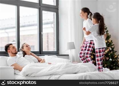 family, winter holidays and people concept - happy daughters wake their mother and father in christmas morning and jumping on bed. happy children wake their parents on christmas