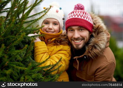 family, winter holidays and people concept - happy father and little daughter choosing christmas tree at street market. happy family choosing christmas tree at market