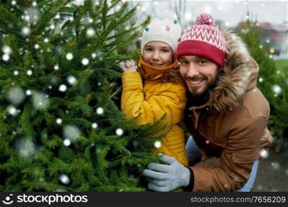 family, winter holidays and people concept - happy father and little daughter choosing christmas tree at street market over snow. happy family choosing christmas tree at market