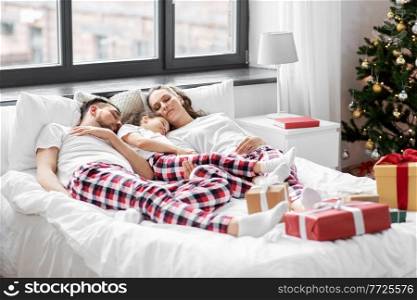 family, winter holidays and people concept - happy little daughter, mother and father in matching pajamas sleeping in bed on christmas morning. happy family sleeping in bed on christmas morning