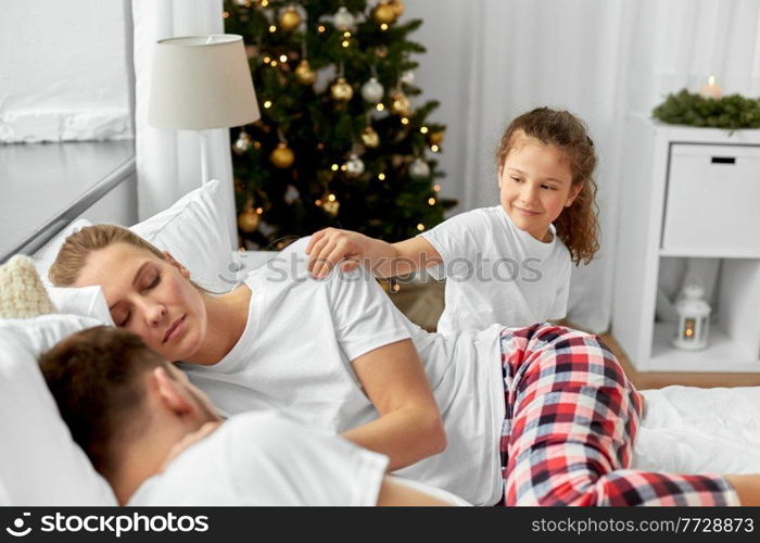 family, winter holidays and people concept - happy little daughter wakes her mother and father in christmas morning. happy girl wakes her parents in christmas morning