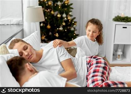 family, winter holidays and people concept - happy little daughter wakes her mother and father in christmas morning. happy girl wakes her parents in christmas morning