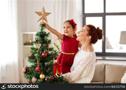 family, winter holidays and people concept - happy mother and little daughter decorating christmas tree at home. mother and daughter decorating christmas tree