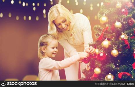 family, winter holidays and people concept - happy mother and little daughter decorating christmas tree. mother and daughter decorating christmas tree