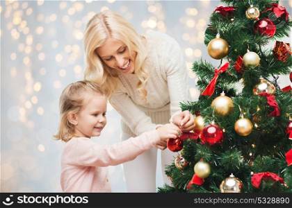 family, winter holidays and people concept - happy mother and little daughter decorating christmas tree. mother and daughter decorating christmas tree
