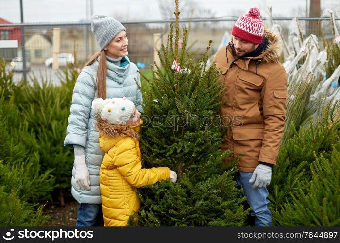 family, winter holidays and people concept - happy mother, father and little daughter choosing christmas tree at street market. happy family choosing christmas tree at market