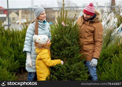 family, winter holidays and people concept - happy mother, father and little daughter choosing christmas tree at street market. happy family choosing christmas tree at market