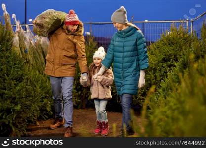 family, winter holidays and people concept - happy mother, father and little daughter buying christmas tree at street market in evening. happy family buying christmas tree at market