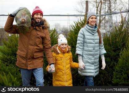 family, winter holidays and people concept - happy mother, father and little daughter buying christmas tree at street market. happy family buying christmas tree at market