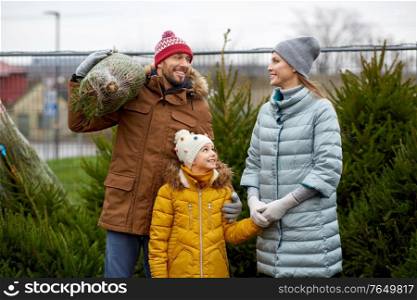 family, winter holidays and people concept - happy mother, father and little daughter buying christmas tree at street market. happy family buying christmas tree at market