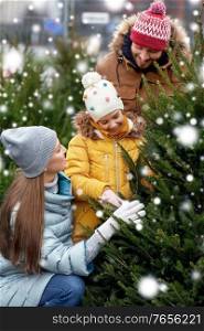 family, winter holidays and people concept - happy mother, father and little daughter choosing christmas tree at street market over snow. happy family choosing christmas tree at market