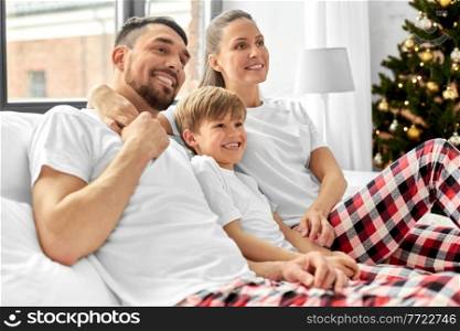 family, winter holidays and people concept - happy mother, father and little son in matching pajamas sitting in bed in christmas morning. family in pajamas in bed in christmas morning