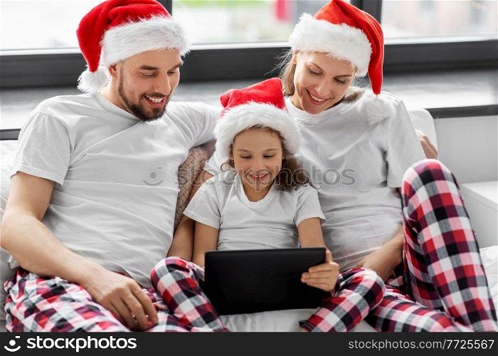 family, winter holidays and people concept - happy mother, father and little daughter with tablet pc computer in bed at home on christmas. happy family with tablet pc in bed on christmas