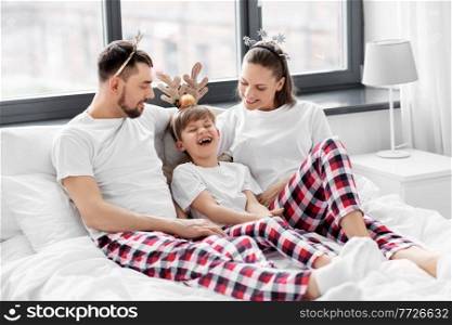 family, winter holidays and people concept - happy mother, father and little son in matching pajamas sitting in bed in christmas morning. family in pajamas in bed in christmas morning
