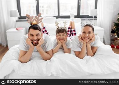 family, winter holidays and people concept - happy mother, father and little son in pajamas sitting in bed in christmas morning. family in pajamas in bed in christmas morning