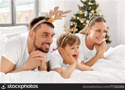 family, winter holidays and people concept - happy mother, father and little son in bed in christmas morning. family in bed in christmas morning
